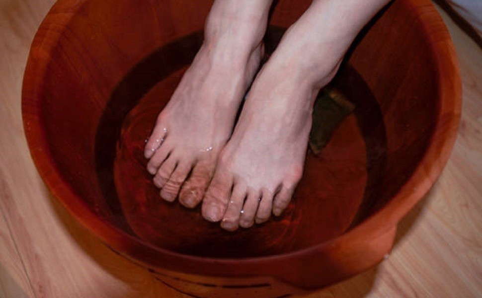 A woman soaks her feet in a deep reddish brown foot bath